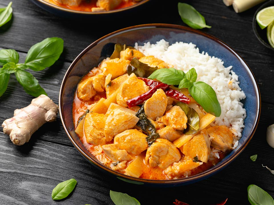 Ein Teller voll Chicken-Curry mit Reis, in dem Ingwer und Kurkuma als Zutanten verwendet wurde steht auf einem Tisch.