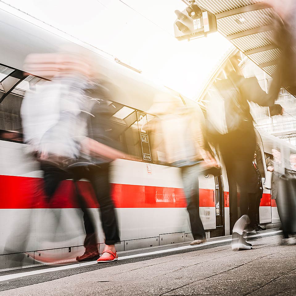 Ein ICE fährt an einem Bahnhof ein und es tummeln sich viele Menschen dort.